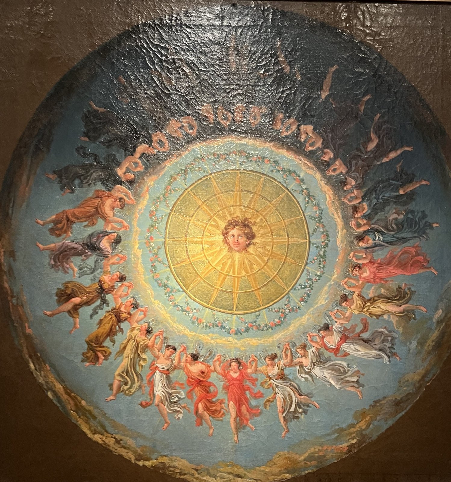 Tecto pintado com um medalhão circular: um rosto solar ao centro, ninfas e figuras dançantes em redor.