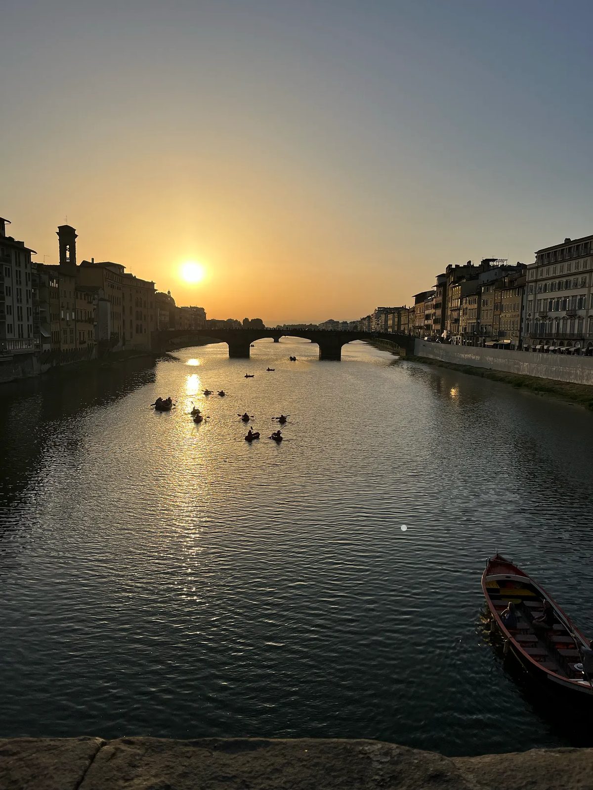 O Arno ao pôr do sol, com a ponte e barcos na água.