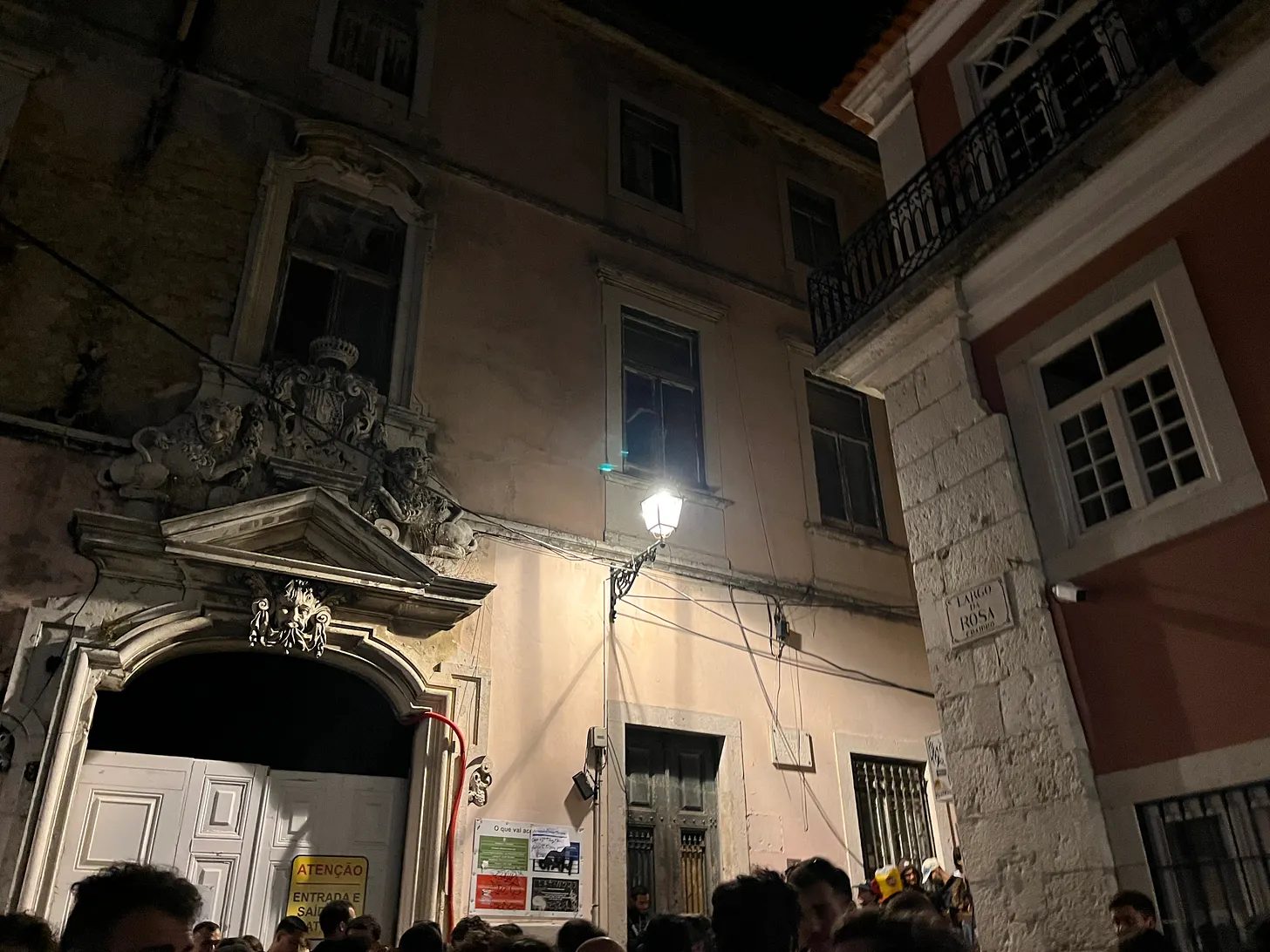 Portal barroco iluminado à noite, com público reunido em baixo.