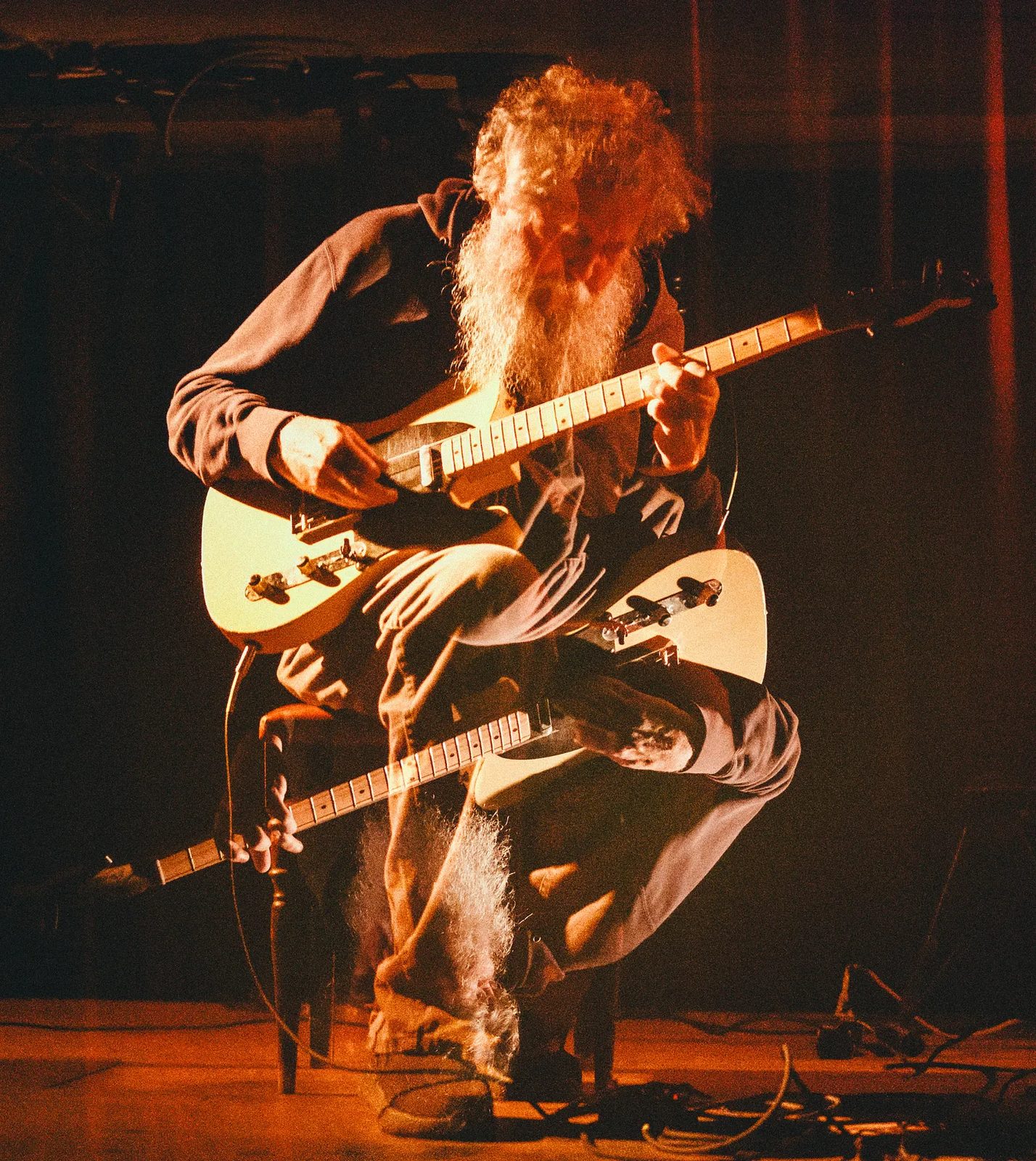 Bill Orcutt em palco, de guitarra branca, sob luz vermelha.