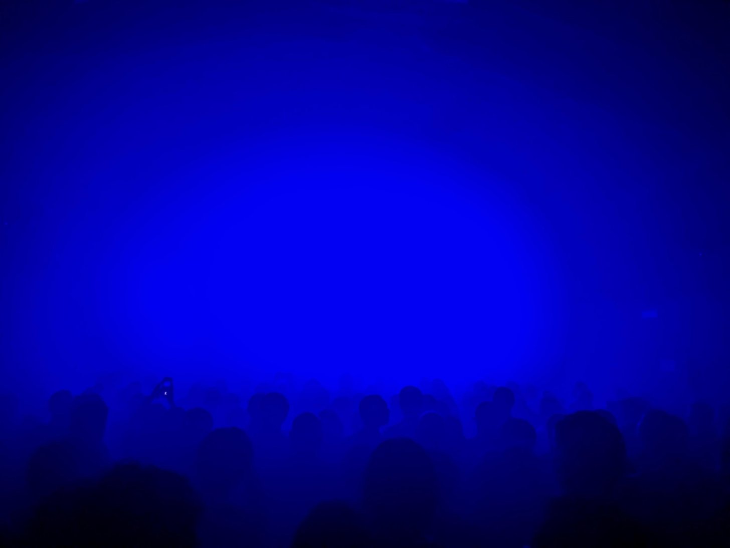 O palco inundado de luz azul, com o público em silhueta.
